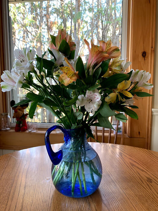 A blue glass vase of flowers against a window.